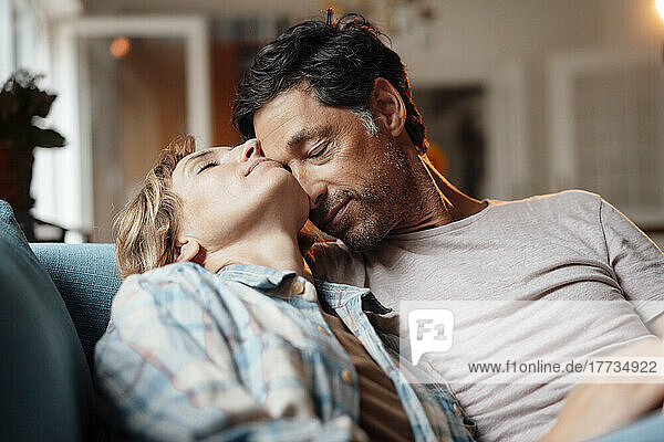 Mature man with eyes closed embracing woman sitting on sofa at home