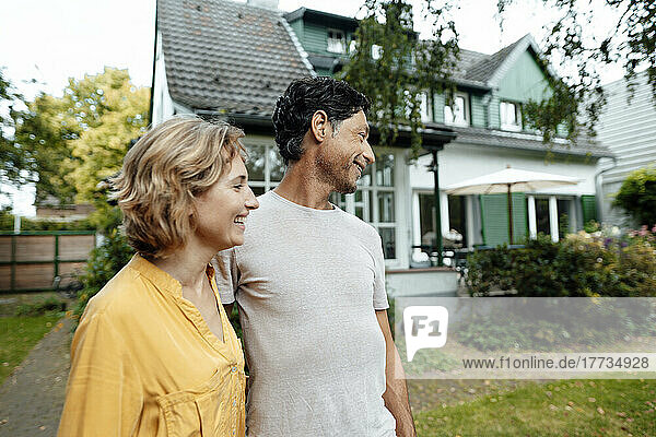 Happy mature man and woman standing in front of house