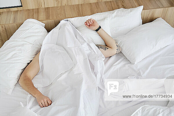 Young man sleeping under blanket in bed at home