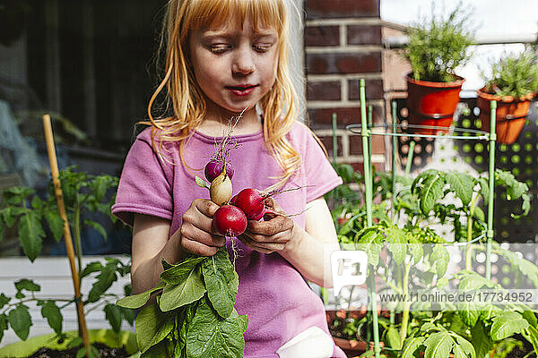 Girl with red hair holding fresh radish on balcony