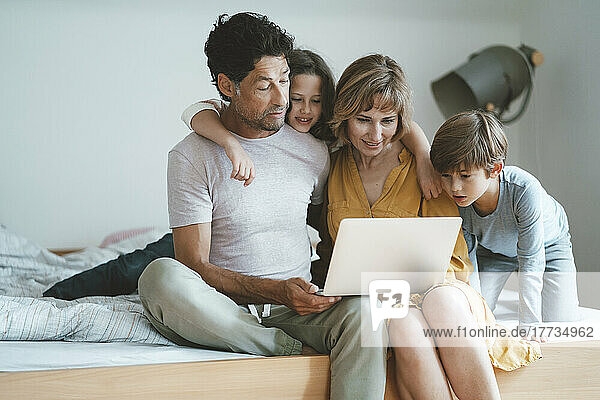 Family sharing laptop sitting on bed at home