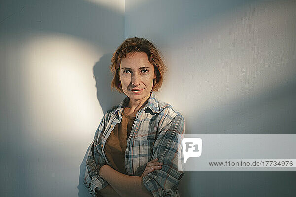 Smiling woman with arms crossed standing in front of wall