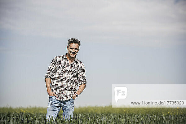 Happy mature man with hands in pockets standing at field on sunny day