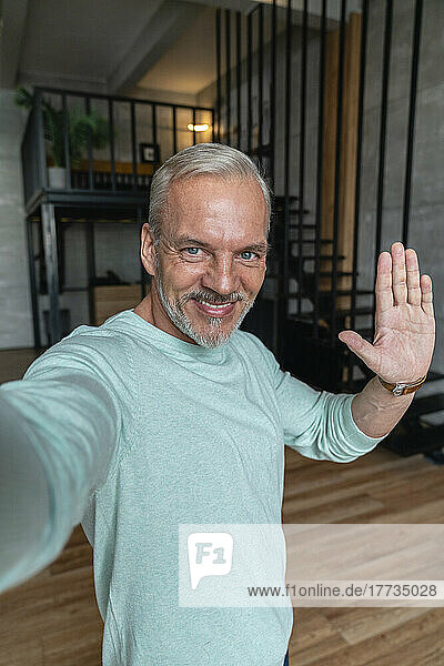 Lächelnder Mann gestikuliert und macht zu Hause ein Selfie