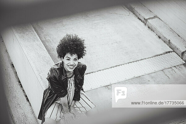 Cheerful young woman with Afro hairstyle sitting on wall