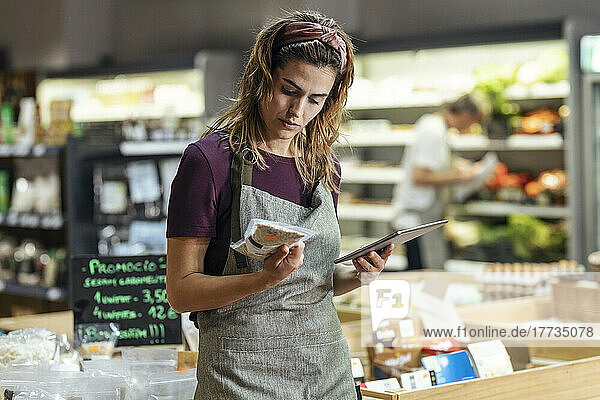 Shop owner holding tablet PC analyzing product at organic market