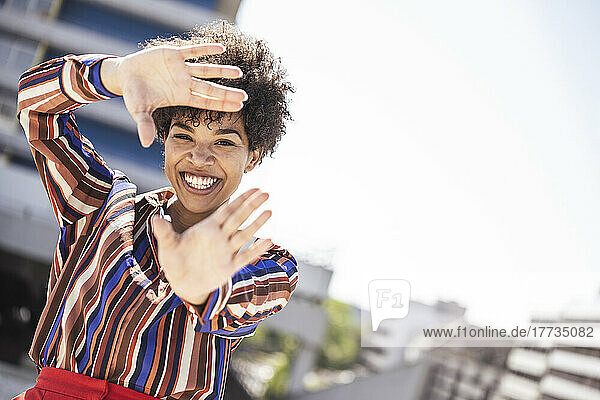 Cheerful woman gesturing hand frame on sunny day