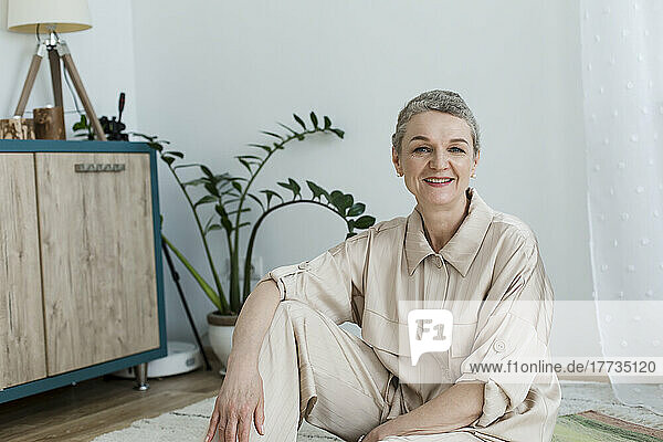 Portrait of smiling mature woman sitting on the floor at home