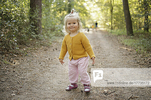 Smiling cute blond girl on footpath in forest