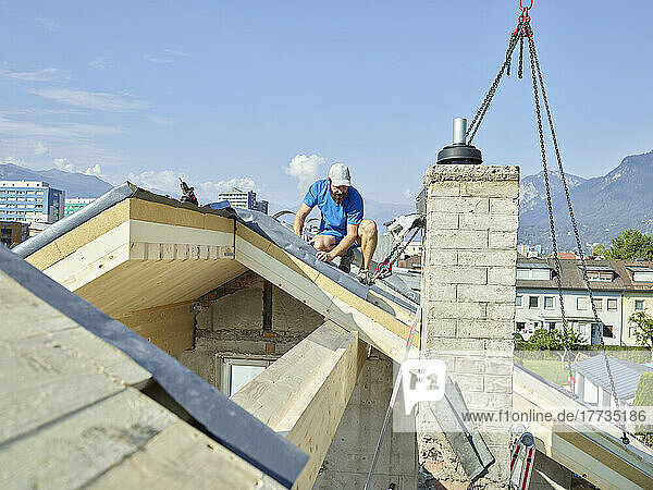 Junger Mann installiert Holzbrett auf Dach mit Kranmaschine