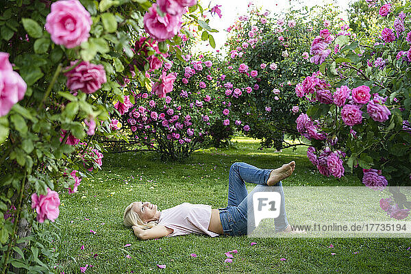 Smiling woman relaxing by lying down on grass at rose garden