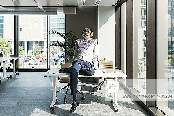 Businessman wearing wireless headphones sitting on desk in office