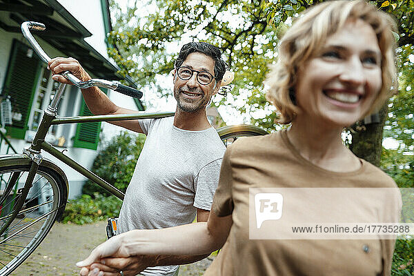 Mature woman with man carrying bicycle on shoulder in back yard
