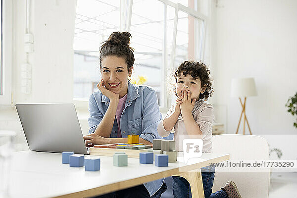 Mother working from home using laptop while daughter is playing with buiilding blocks