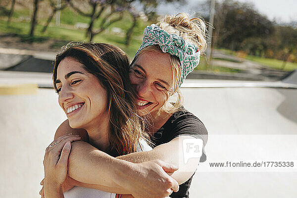 Smiling woman embracing friend from behind on sunny day