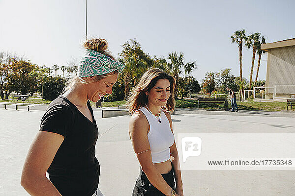 Happy friends talking at skateboard park on sunny day