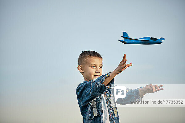 Junge spielt mit blauem Spielzeugflugzeug vor dem Himmel bei Sonnenuntergang