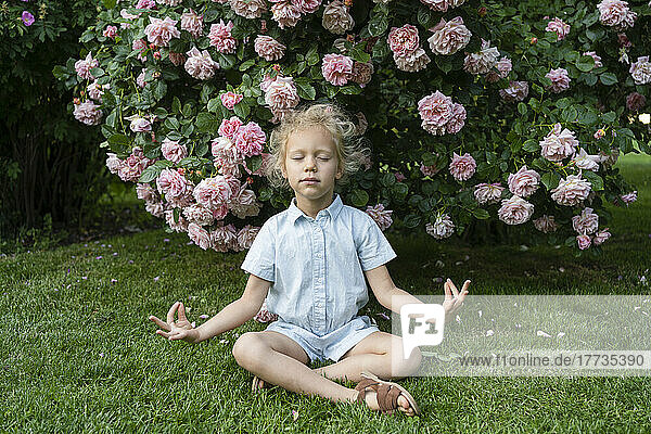 Girl with eyes closed meditating sitting on grass at rose garden
