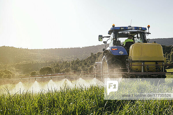 Young farmer spraying fertilizer through sprayer on tractor on field