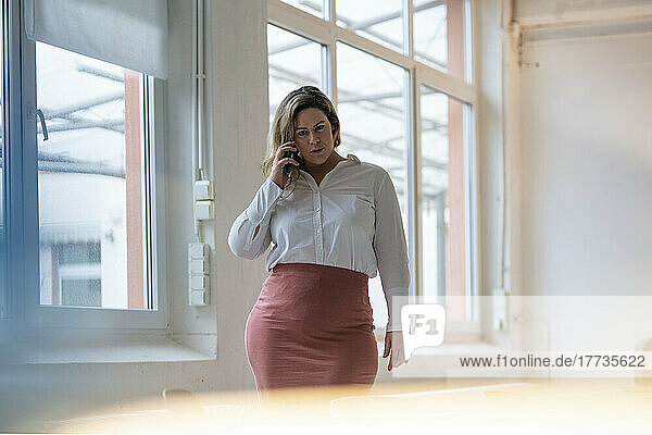 Confident plus size businesswoman talking on smart phone at work place