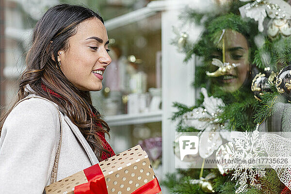 Lächelnde Frau mit Weihnachtsgeschenk beim Schaufensterbummel