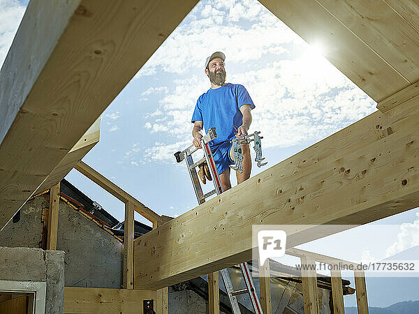 Junger Mann steht an sonnigem Tag auf einer Leiter auf der Baustelle