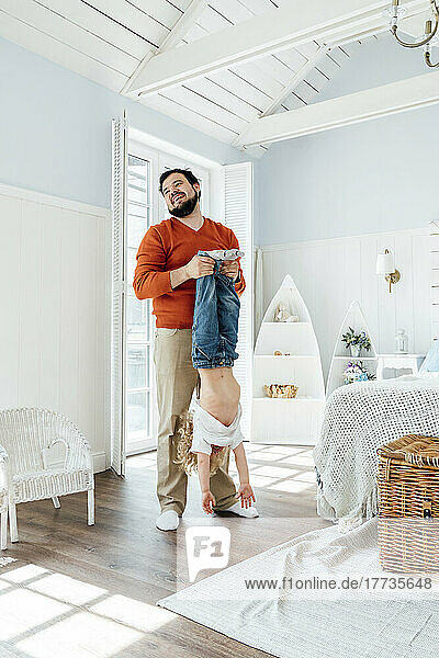 Happy father holding son upside down standing in bedroom at home