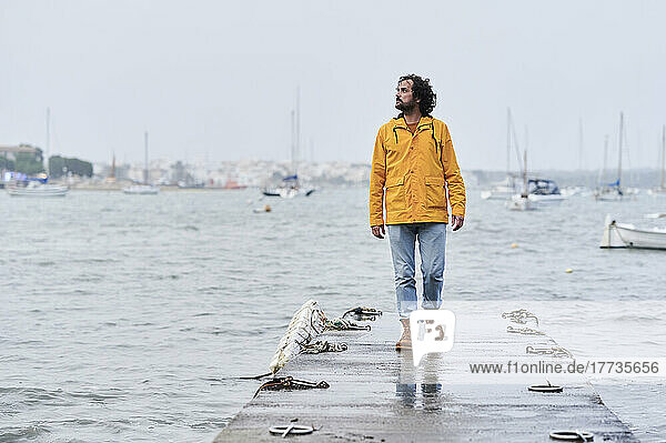 Man wearing yellow raincoat walking on jetty