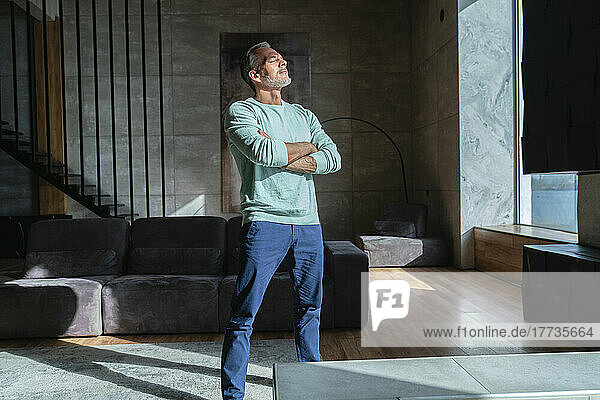 Man standing with arms crossed enjoying sunlight at home