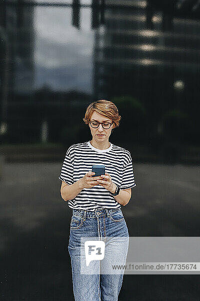 Woman using smart phone standing in front of black wall