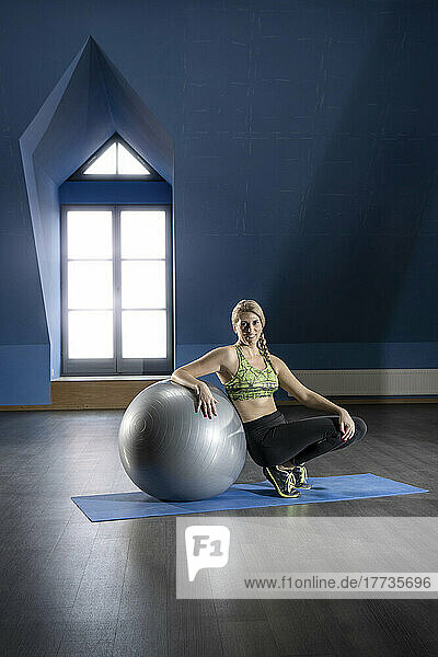 Woman sitting by exercise ball in fitness room