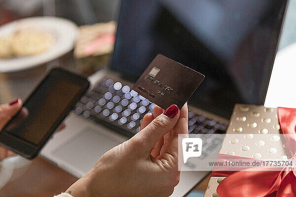 Hands of woman holding credit card and smart phone by Christmas present at home