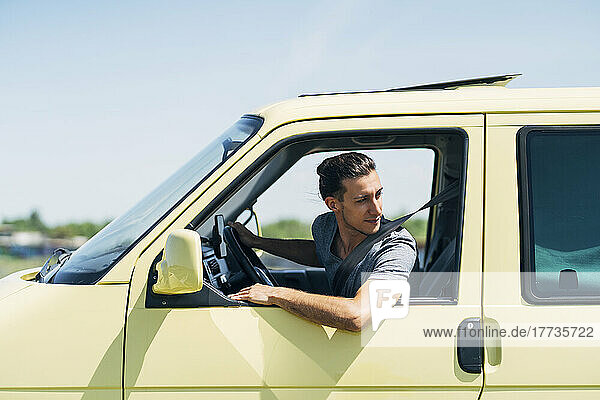 Young man looking out of van's window on sunny day
