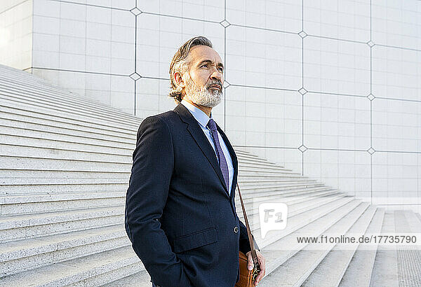 Thoughtful mature businessman with bag standing on steps