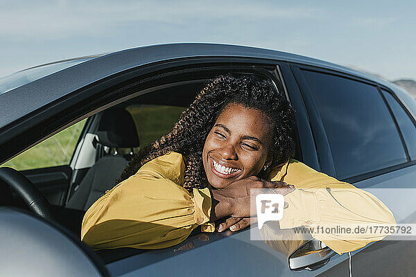 Happy woman leaning out of car's window on sunny day