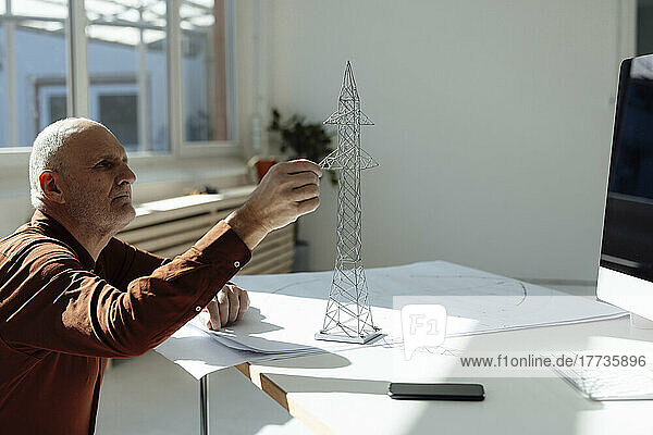 Businessman analyzing electricity pylon model on blueprint at desk