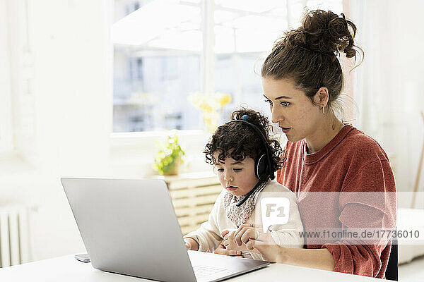 Kleines Mädchen mit Headset sitzt auf dem Schoß der Mutter und benutzt Laptop