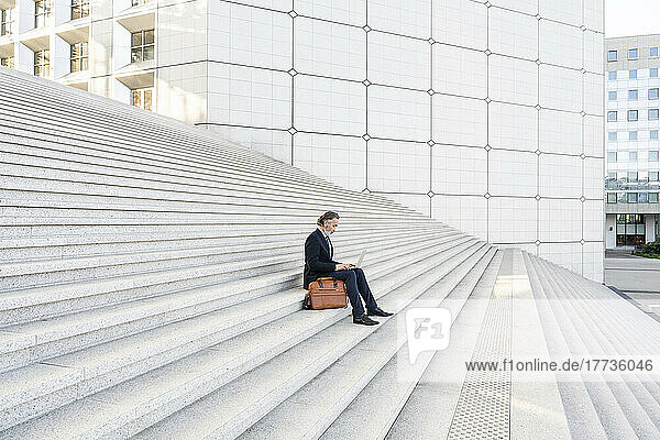 Mature businessman using laptop sitting on staircase