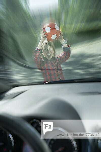 Scared boy with ball seen through windshield of car trying to prevent accident