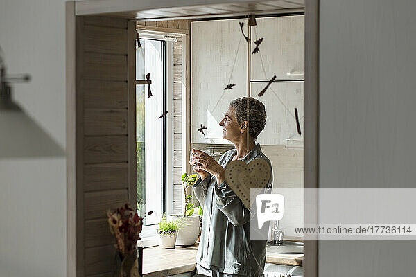 Mature woman holding tea glass in kitchen at home