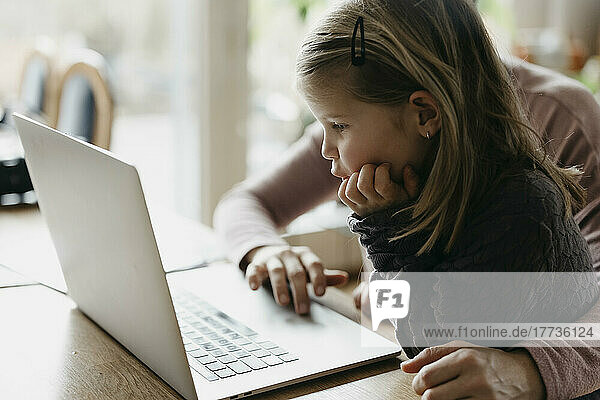 Girl with hand on chin looking at laptop sitting with mother