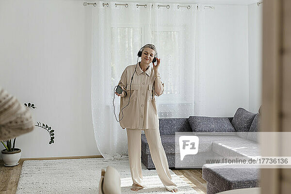 Mature woman wearing headphones listening to music at home