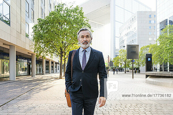 Mature businessman with hand in pocket walking at office park