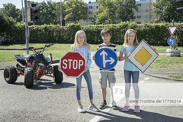Smiling children holding road signs board on standing road