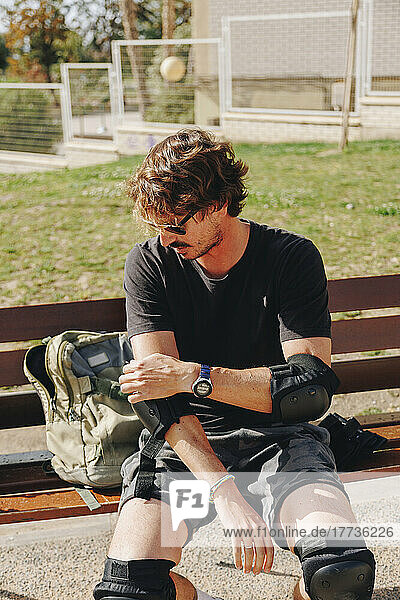 Man sitting on bench adjusting elbow pad at park