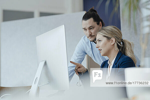 Geschäftsfrau bei Treffen mit Kollege zeigt auf Desktop-PC