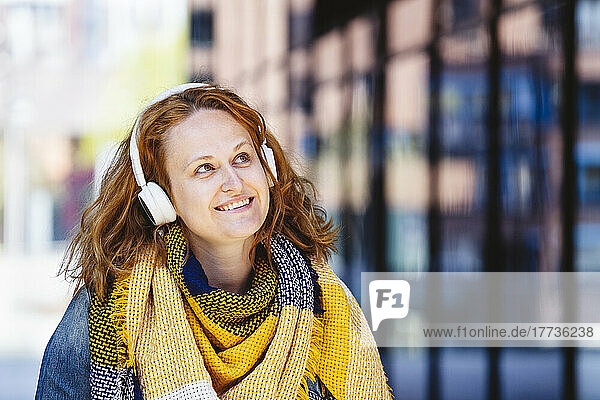 Happy woman wearing yellow plaid scarf listening music through headphones