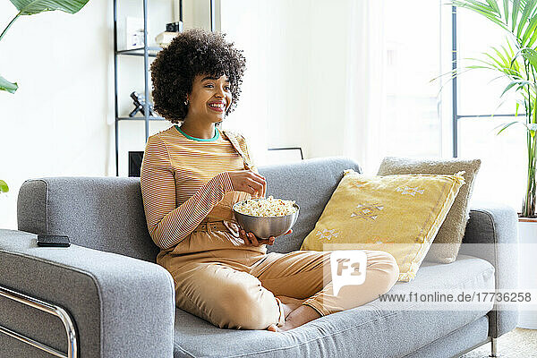 Happy woman holding popcorn bowl sitting on sofa