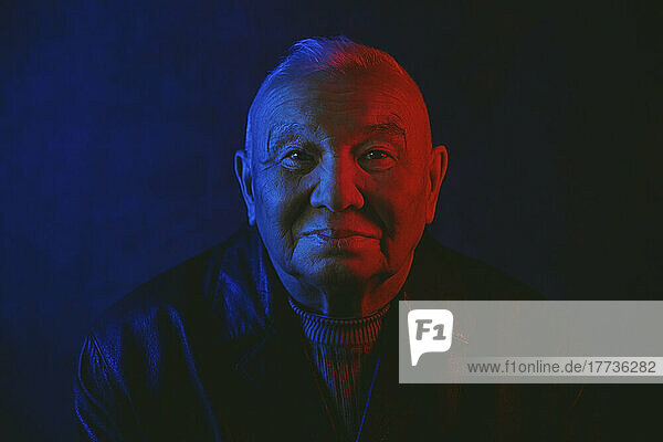 Senior man's face illuminated with red and blue neon light against black background