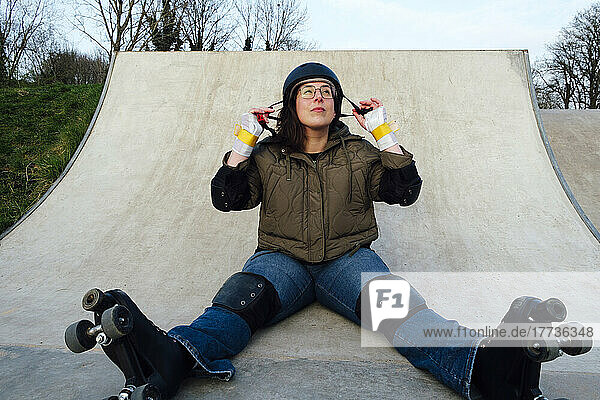 Woman with roller skates sitting on ramp in skate park